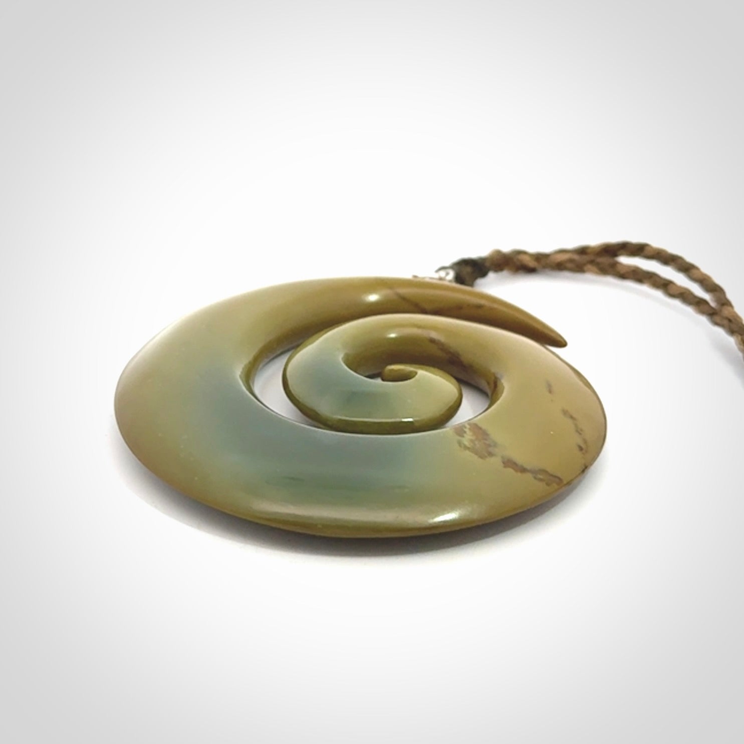 This picture shows a large hand-carved koru. It is carved from New Zealand flower jade and is suspended from an adjustable cord.