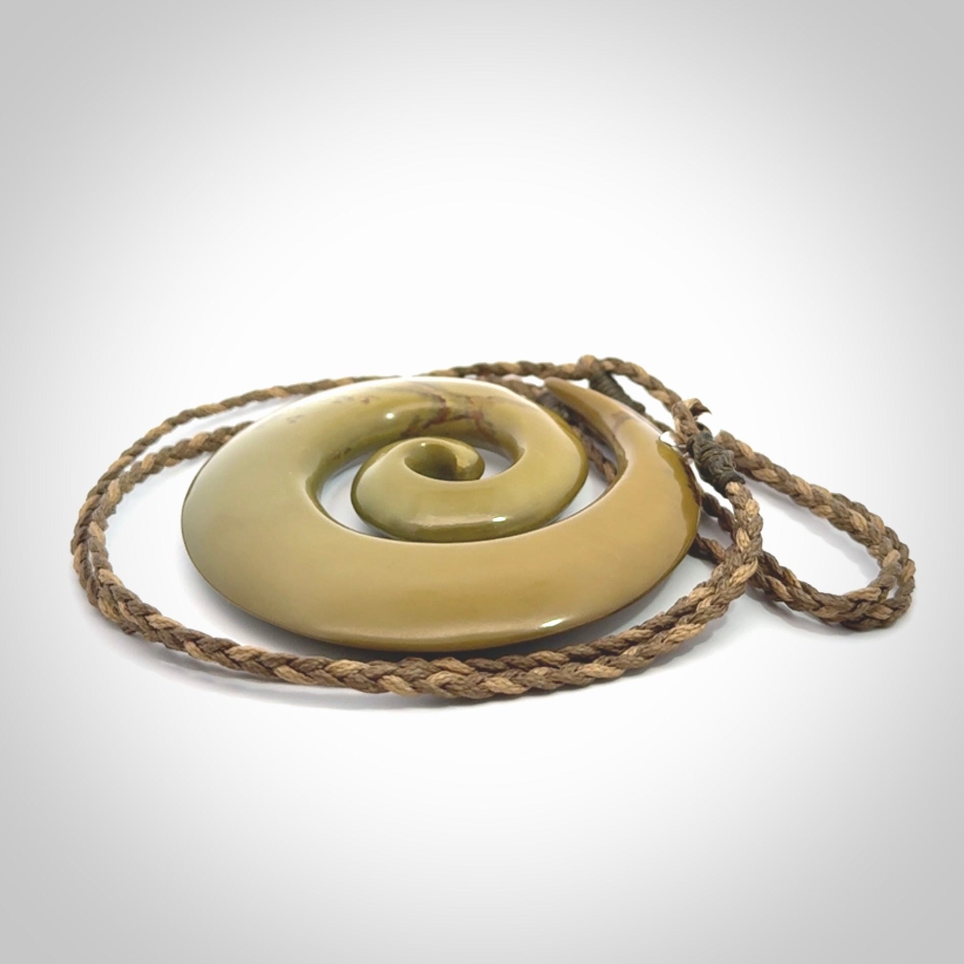 This picture shows a large hand-carved koru. It is carved from New Zealand flower jade and is suspended from an adjustable cord.
