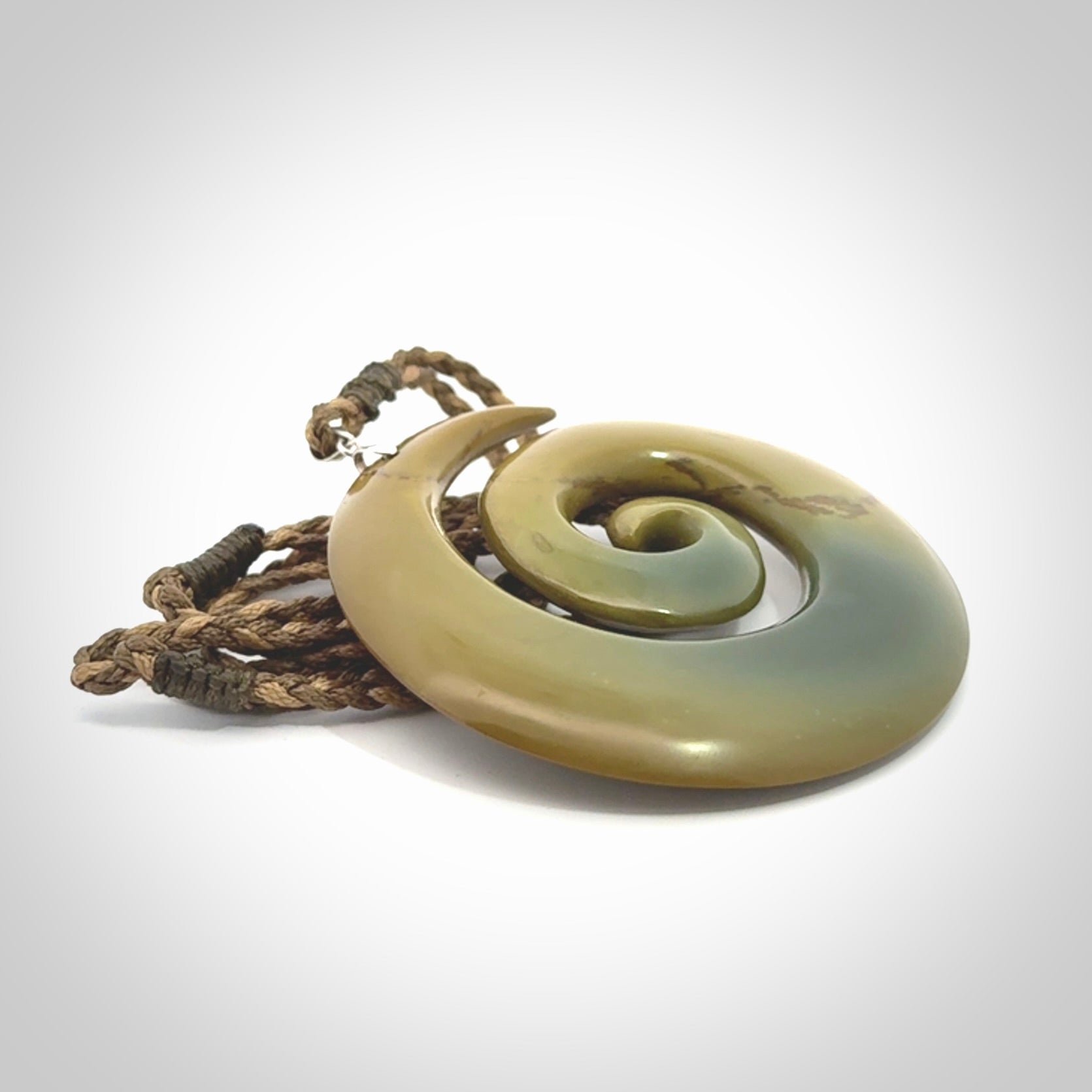 This picture shows a large hand-carved koru. It is carved from New Zealand flower jade and is suspended from an adjustable cord.