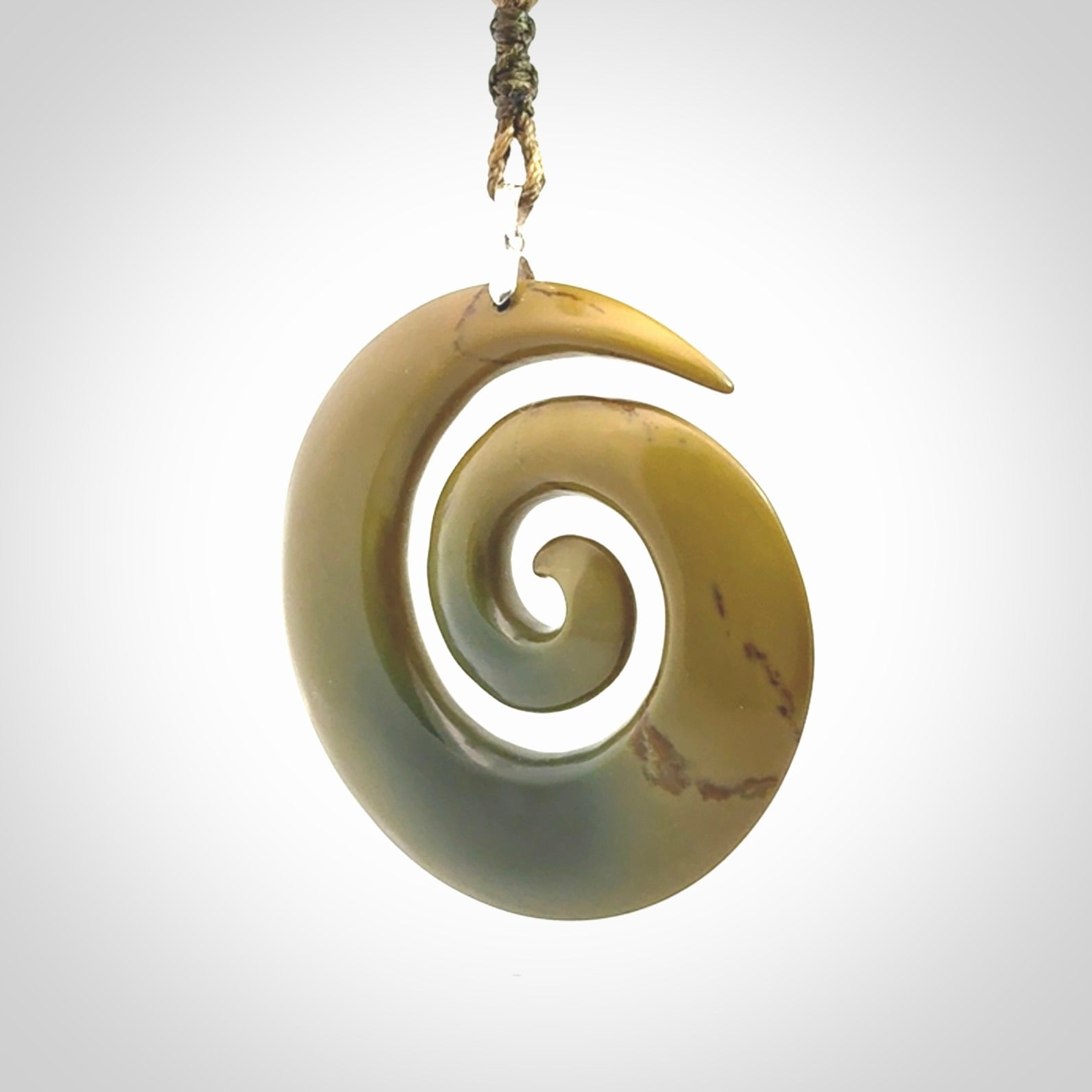 This picture shows a large hand-carved koru. It is carved from New Zealand flower jade and is suspended from an adjustable cord.