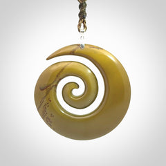 This picture shows a large hand-carved koru. It is carved from New Zealand flower jade and is suspended from an adjustable cord.