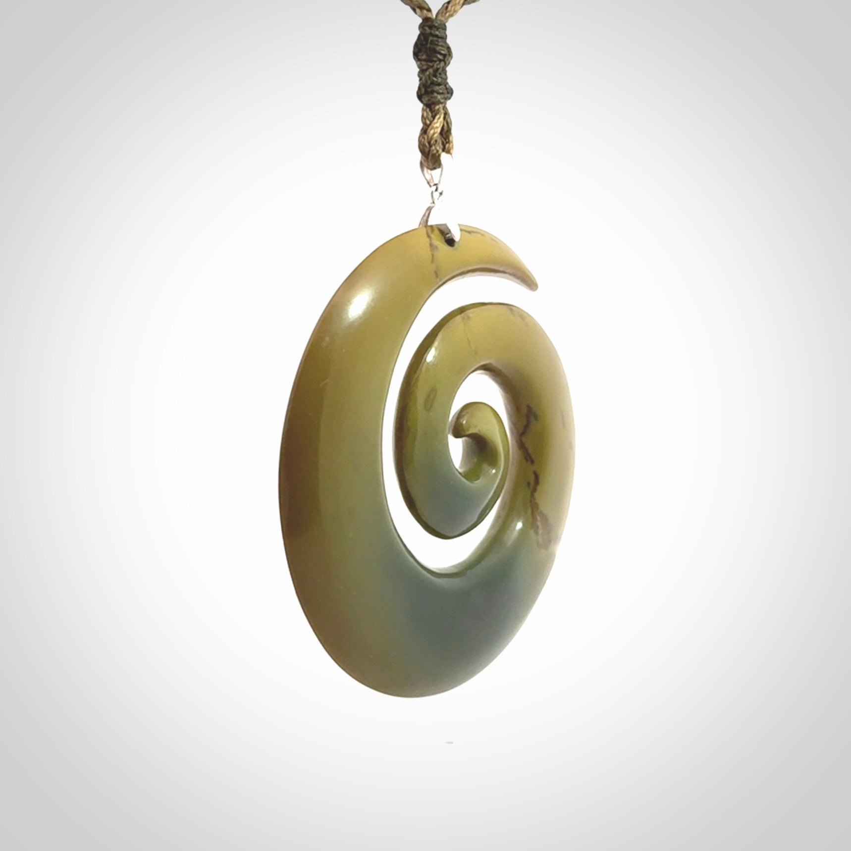 This picture shows a large hand-carved koru. It is carved from New Zealand flower jade and is suspended from an adjustable cord.