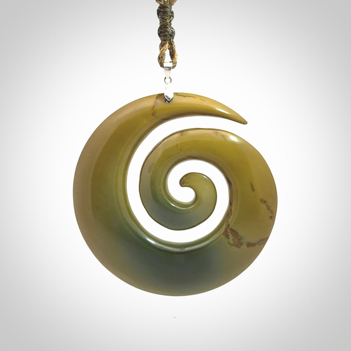 This picture shows a large hand-carved koru. It is carved from New Zealand flower jade and is suspended from an adjustable cord.