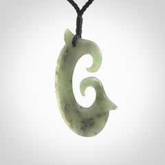 This picture shows a large hand-carved contemporary koru pendant. It is carved from New Zealand Kokopu jade and is suspended from a hand-plaited, black cord.