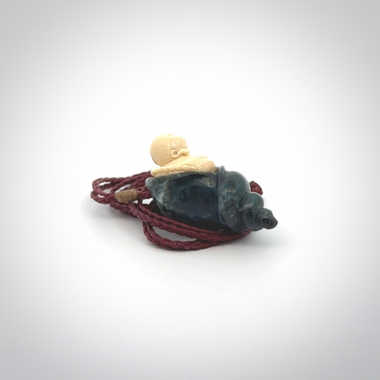This photo shows a Buddha pendant hand carved in Woolly Mammoth Tusk with Moss Agate. It is provided with an adjustable plum cord.