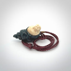 This photo shows a Buddha pendant hand carved in Woolly Mammoth Tusk with Moss Agate. It is provided with an adjustable plum cord.