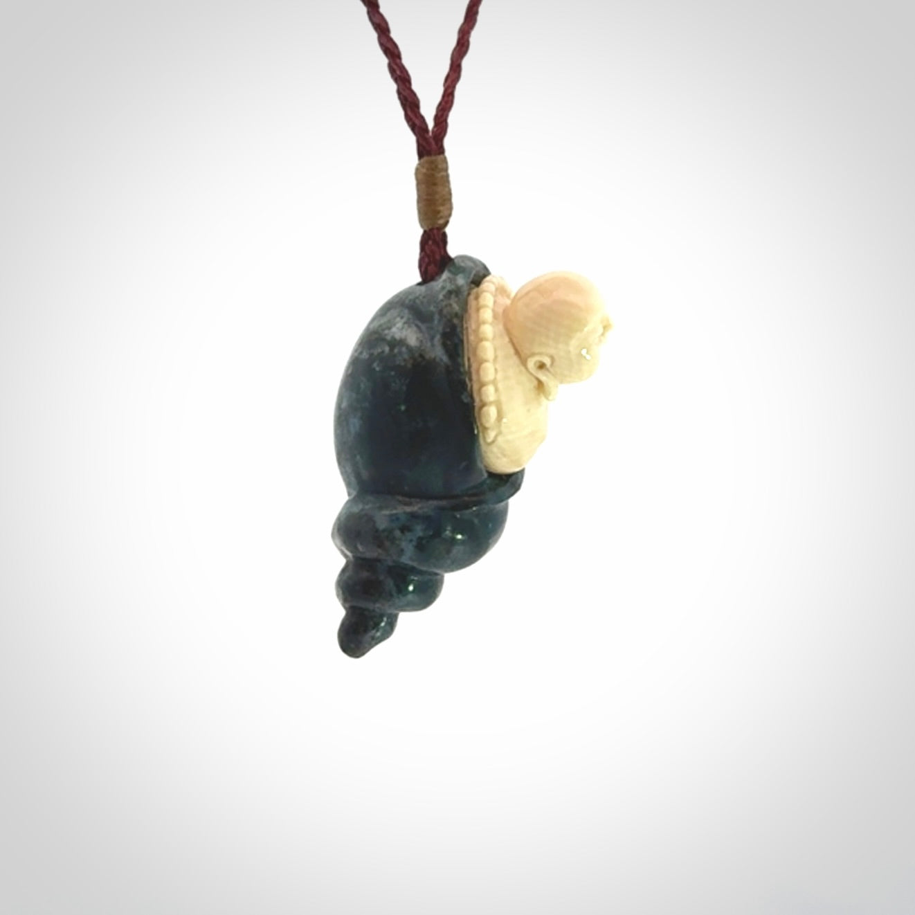 This photo shows a Buddha pendant hand carved in Woolly Mammoth Tusk with Moss Agate. It is provided with an adjustable plum cord.