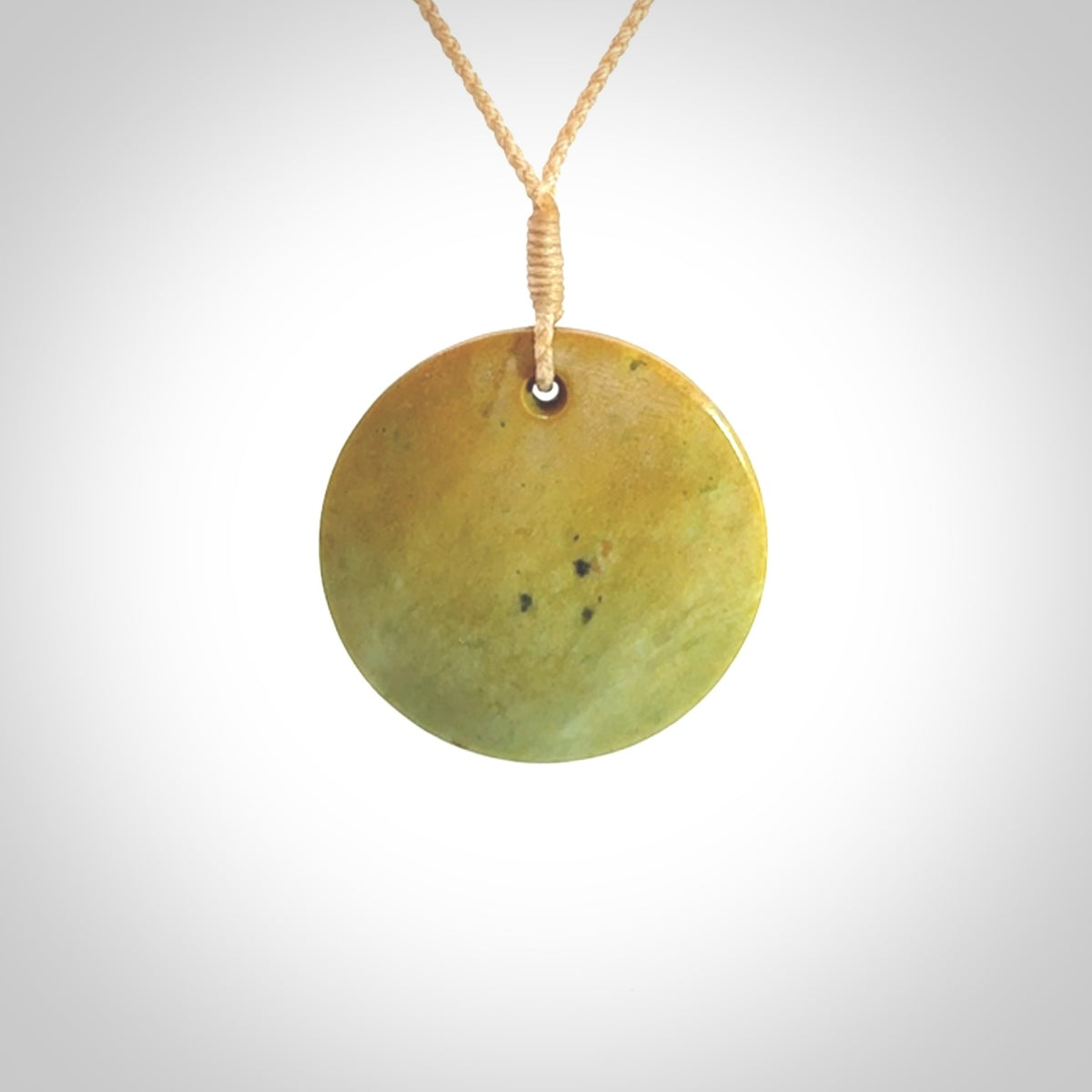 This piece is a oval round, disc pendant carved in New Zealand Flower Jade. It is suspended on a beige coloured braided cord that is length adjustable.