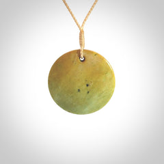 This piece is a oval round, disc pendant carved in New Zealand Flower Jade. It is suspended on a beige coloured braided cord that is length adjustable.