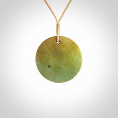 This piece is a oval round, disc pendant carved in New Zealand Flower Jade. It is suspended on a beige coloured braided cord that is length adjustable.