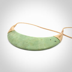 This picture shows a hand carved New Zealand jade contemporary half-shield pendant. It is a light green colour and is a wonderful, large piece of jewellery. The cord is hand plaited and adjustable so that you can position the pendant where it suits you best. This piece was carved for us by Donna Summers.
