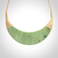 This picture shows a hand carved New Zealand jade contemporary half-shield pendant. It is a light green colour and is a wonderful, large piece of jewellery. The cord is hand plaited and adjustable so that you can position the pendant where it suits you best. This piece was carved for us by Donna Summers.