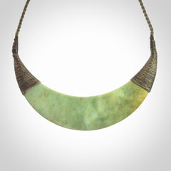 This picture shows a hand carved New Zealand flower jade contemporary half-shield pendant. It is a light green colour and is a wonderful, large piece of jewellery. The cord is hand plaited and adjustable so that you can position the pendant where it suits you best. This piece was carved for us by Donna Summers.