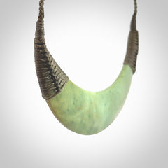 This picture shows a hand carved New Zealand flower jade contemporary half-shield pendant. It is a light green colour and is a wonderful, large piece of jewellery. The cord is hand plaited and adjustable so that you can position the pendant where it suits you best. This piece was carved for us by Donna Summers.