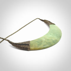 This picture shows a hand carved New Zealand flower jade contemporary half-shield pendant. It is a light green colour and is a wonderful, large piece of jewellery. The cord is hand plaited and adjustable so that you can position the pendant where it suits you best. This piece was carved for us by Donna Summers.