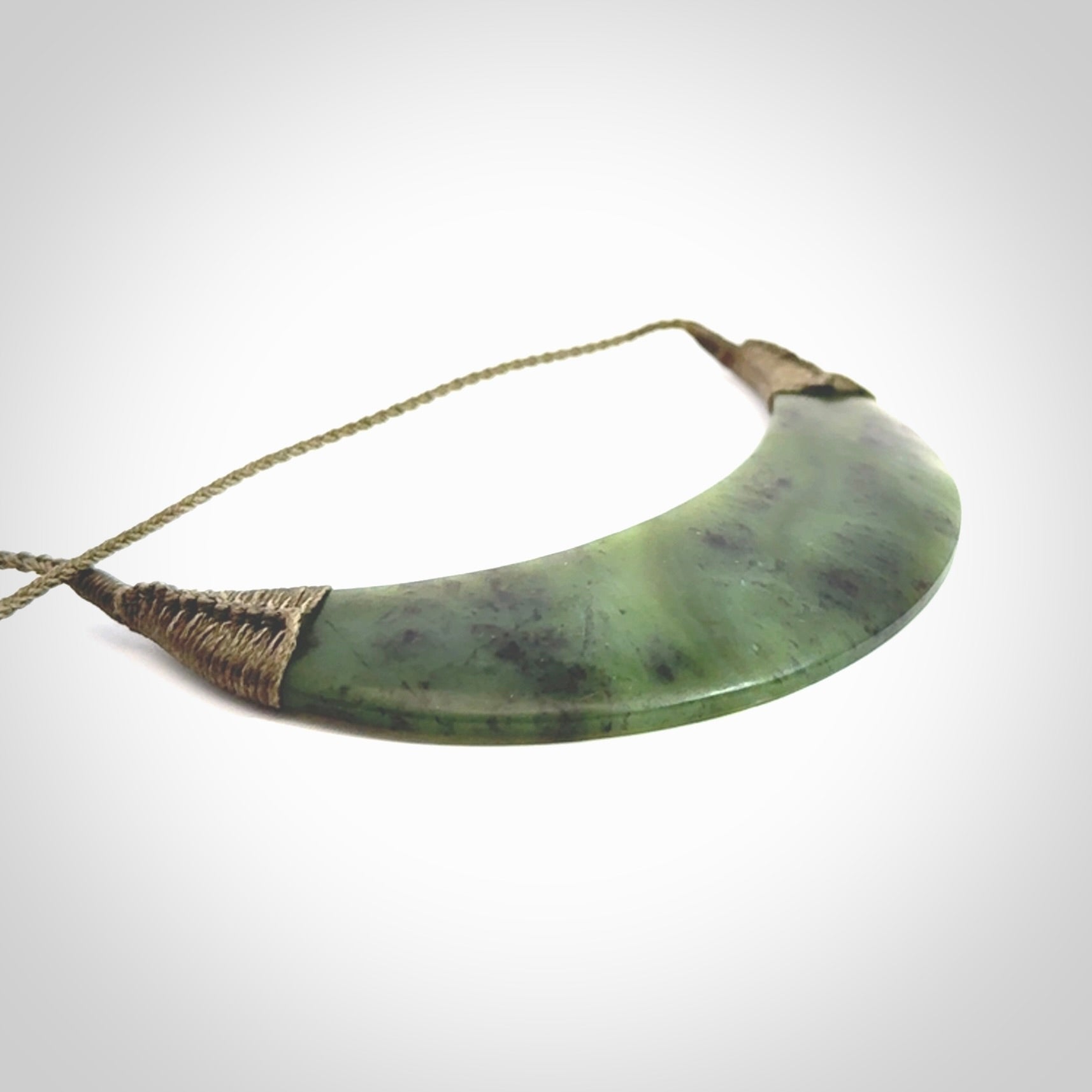 This picture shows a hand carved New Zealand jade contemporary half-shield pendant. It is a semi-transluscent green colour and is a wonderful, large piece of jewellery. The cord is hand plaited and adjustable so that you can position the pendant where it suits you best. This piece was carved for us by Donna Summers.
