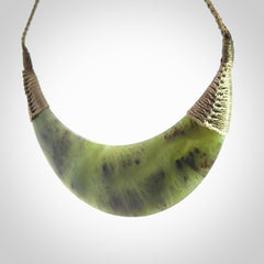 This picture shows a hand carved New Zealand jade contemporary half-shield pendant. It is a semi-transluscent green colour and is a wonderful, large piece of jewellery. The cord is hand plaited and adjustable so that you can position the pendant where it suits you best. This piece was carved for us by Donna Summers.