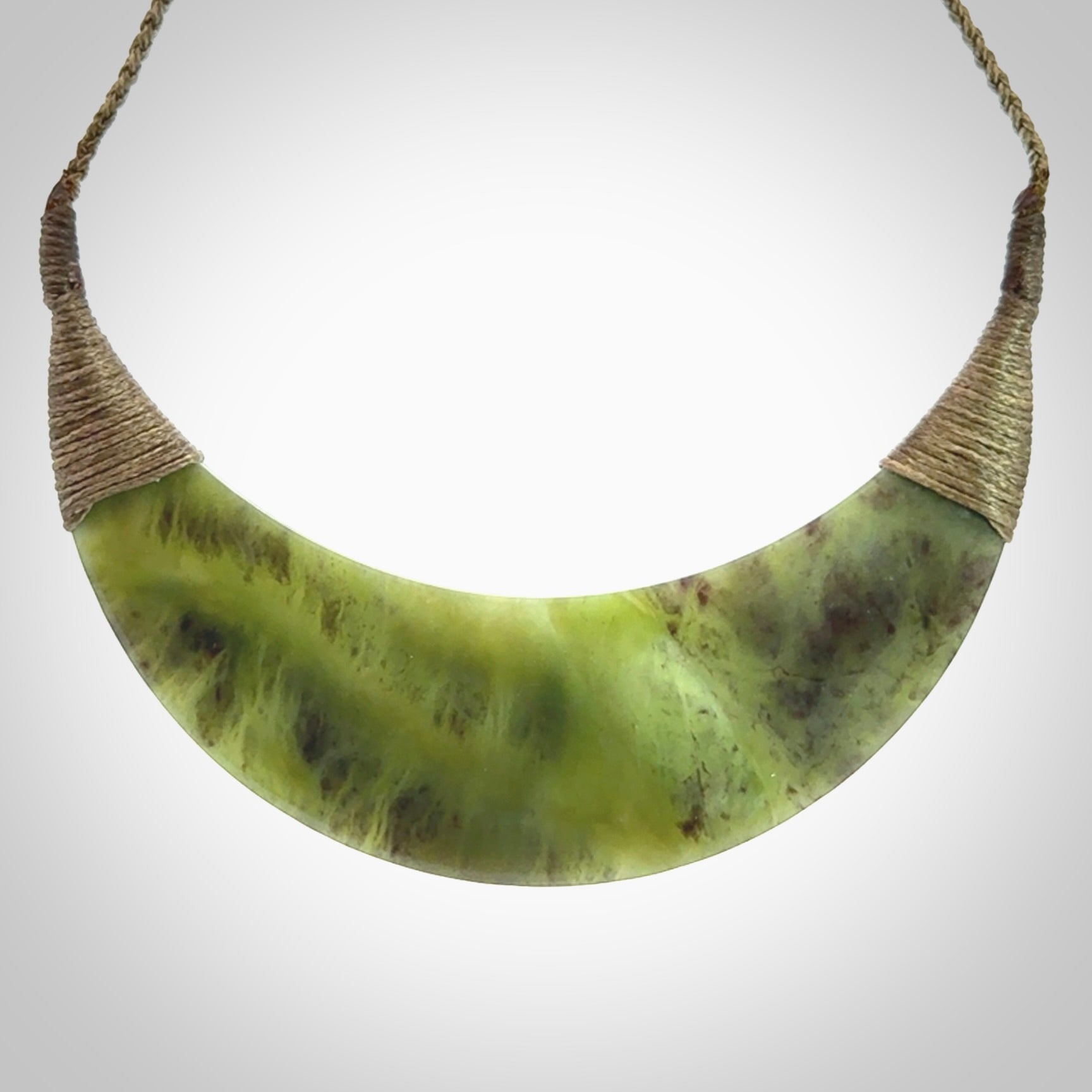 This picture shows a hand carved New Zealand jade contemporary half-shield pendant. It is a semi-transluscent green colour and is a wonderful, large piece of jewellery. The cord is hand plaited and adjustable so that you can position the pendant where it suits you best. This piece was carved for us by Donna Summers.