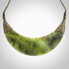 This picture shows a hand carved New Zealand jade contemporary half-shield pendant. It is a semi-transluscent green colour and is a wonderful, large piece of jewellery. The cord is hand plaited and adjustable so that you can position the pendant where it suits you best. This piece was carved for us by Donna Summers.