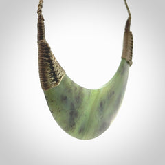 This picture shows a hand carved New Zealand jade contemporary half-shield pendant. It is a semi-transluscent green colour and is a wonderful, large piece of jewellery. The cord is hand plaited and adjustable so that you can position the pendant where it suits you best. This piece was carved for us by Donna Summers.