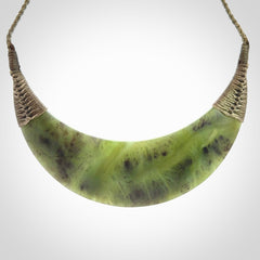 This picture shows a hand carved New Zealand jade contemporary half-shield pendant. It is a semi-transluscent green colour and is a wonderful, large piece of jewellery. The cord is hand plaited and adjustable so that you can position the pendant where it suits you best. This piece was carved for us by Donna Summers.