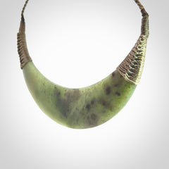 This picture shows a hand carved New Zealand jade contemporary half-shield pendant. It is a semi-transluscent green colour and is a wonderful, large piece of jewellery. The cord is hand plaited and adjustable so that you can position the pendant where it suits you best. This piece was carved for us by Donna Summers.