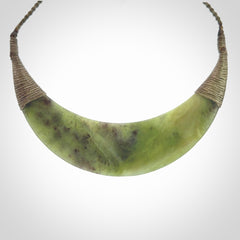 This picture shows a hand carved New Zealand jade contemporary half-shield pendant. It is a semi-transluscent green colour and is a wonderful, large piece of jewellery. The cord is hand plaited and adjustable so that you can position the pendant where it suits you best. This piece was carved for us by Donna Summers.