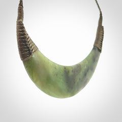 This picture shows a hand carved New Zealand jade contemporary half-shield pendant. It is a semi-transluscent green colour and is a wonderful, large piece of jewellery. The cord is hand plaited and adjustable so that you can position the pendant where it suits you best. This piece was carved for us by Donna Summers.
