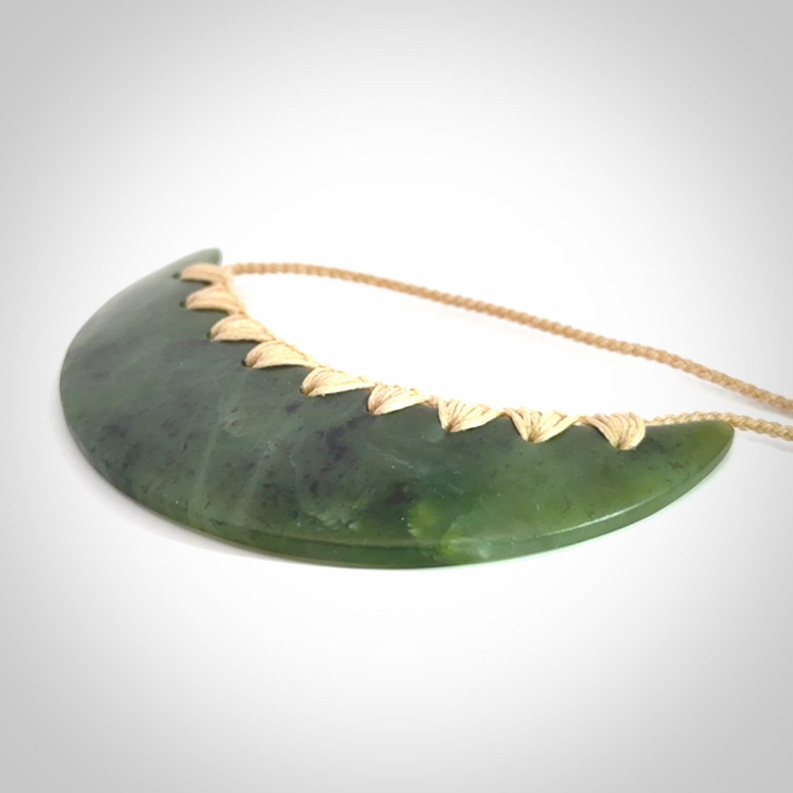 This picture shows a hand carved jade contemporary half-shield pendant. It is a semi-transluscent green colour. The cord is hand plaited and adjustable so that you can position the pendant where it suits you best.