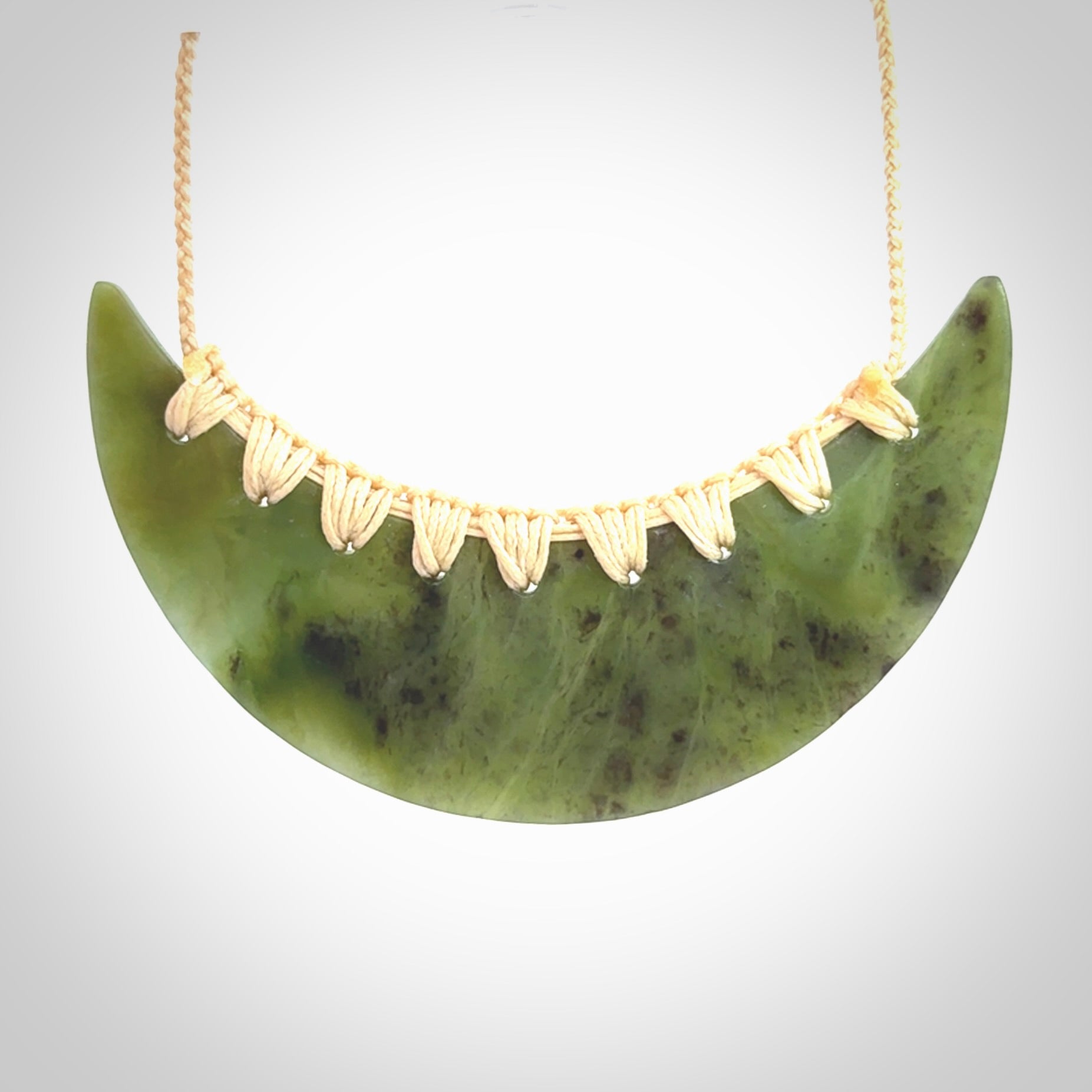 This picture shows a hand carved jade contemporary half-shield pendant. It is a semi-transluscent green colour. The cord is hand plaited and adjustable so that you can position the pendant where it suits you best.
