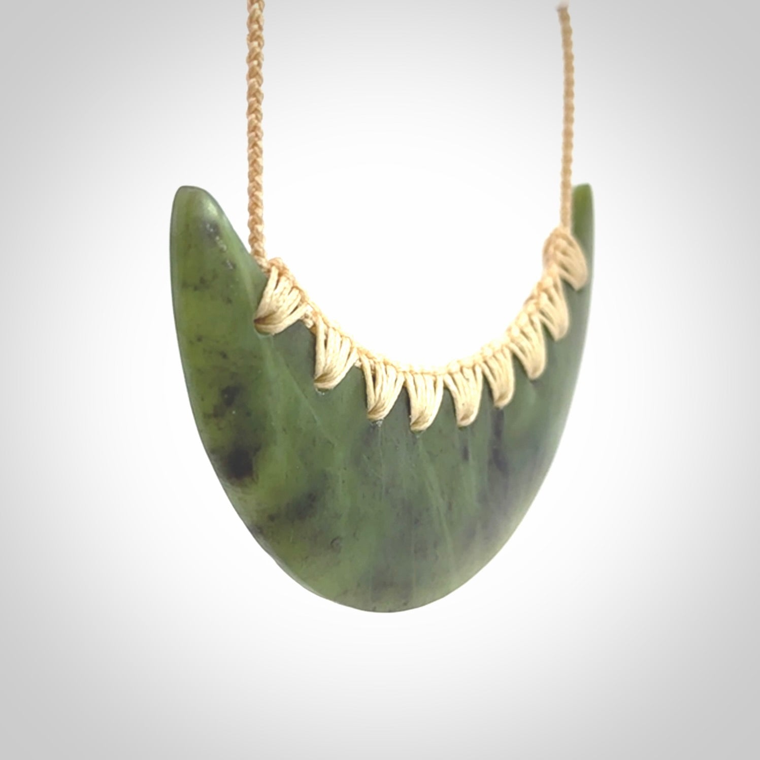 This picture shows a hand carved jade contemporary half-shield pendant. It is a semi-transluscent green colour. The cord is hand plaited and adjustable so that you can position the pendant where it suits you best.