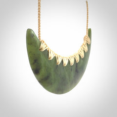 This picture shows a hand carved jade contemporary half-shield pendant. It is a semi-transluscent green colour. The cord is hand plaited and adjustable so that you can position the pendant where it suits you best.