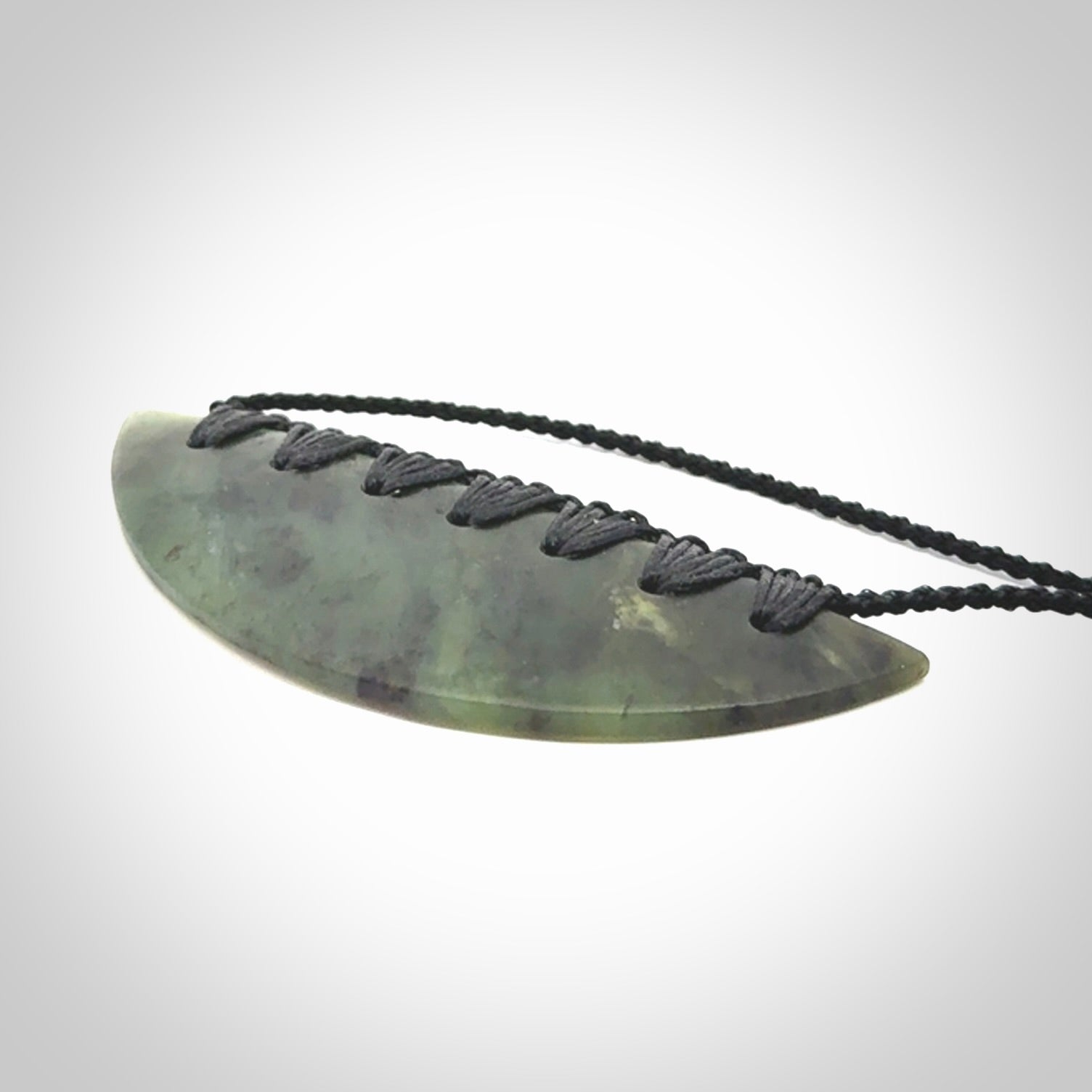 This picture shows a hand carved jade contemporary half-shield pendant. It is a semi-transluscent green colour. The cord is hand plaited and adjustable so that you can position the pendant where it suits you best.