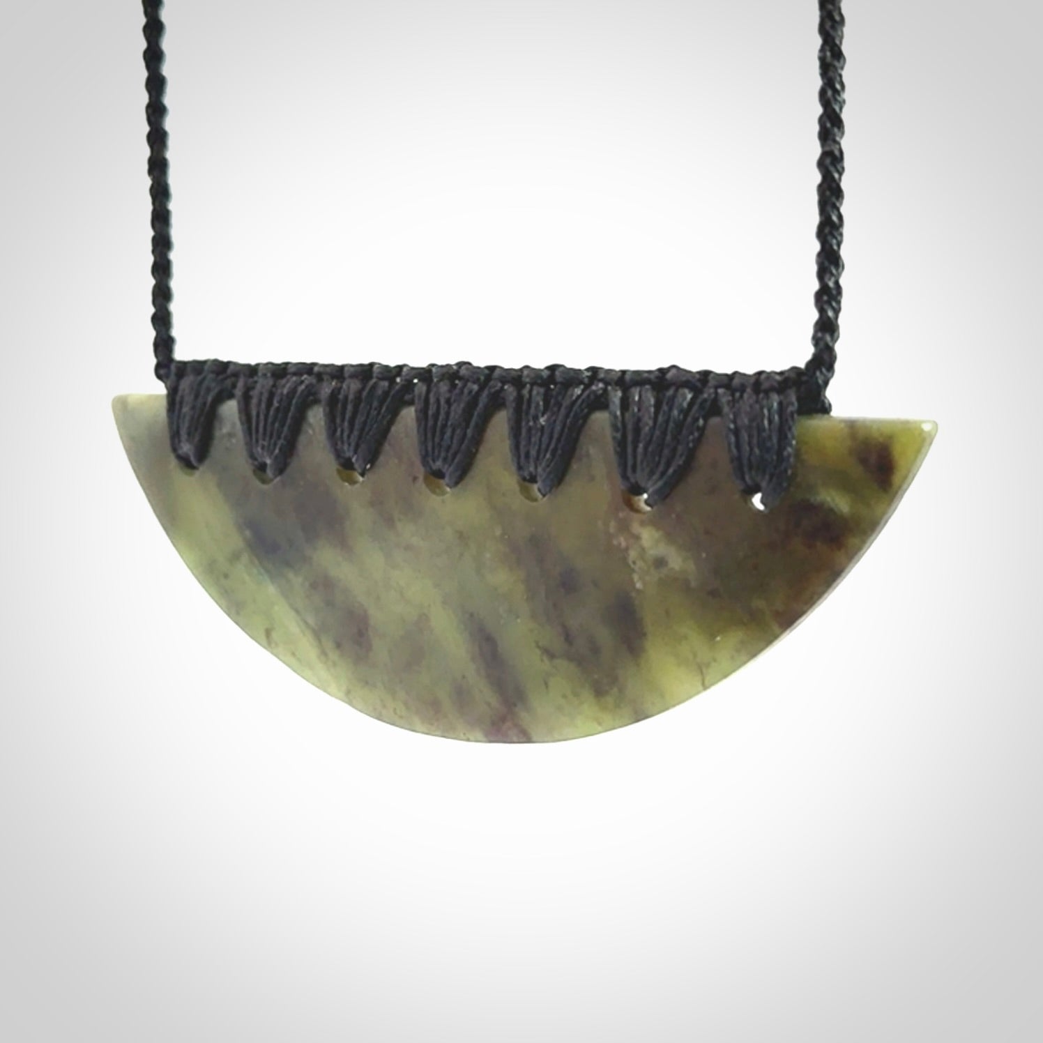 This picture shows a hand carved jade contemporary half-shield pendant. It is a semi-transluscent green colour. The cord is hand plaited and adjustable so that you can position the pendant where it suits you best.