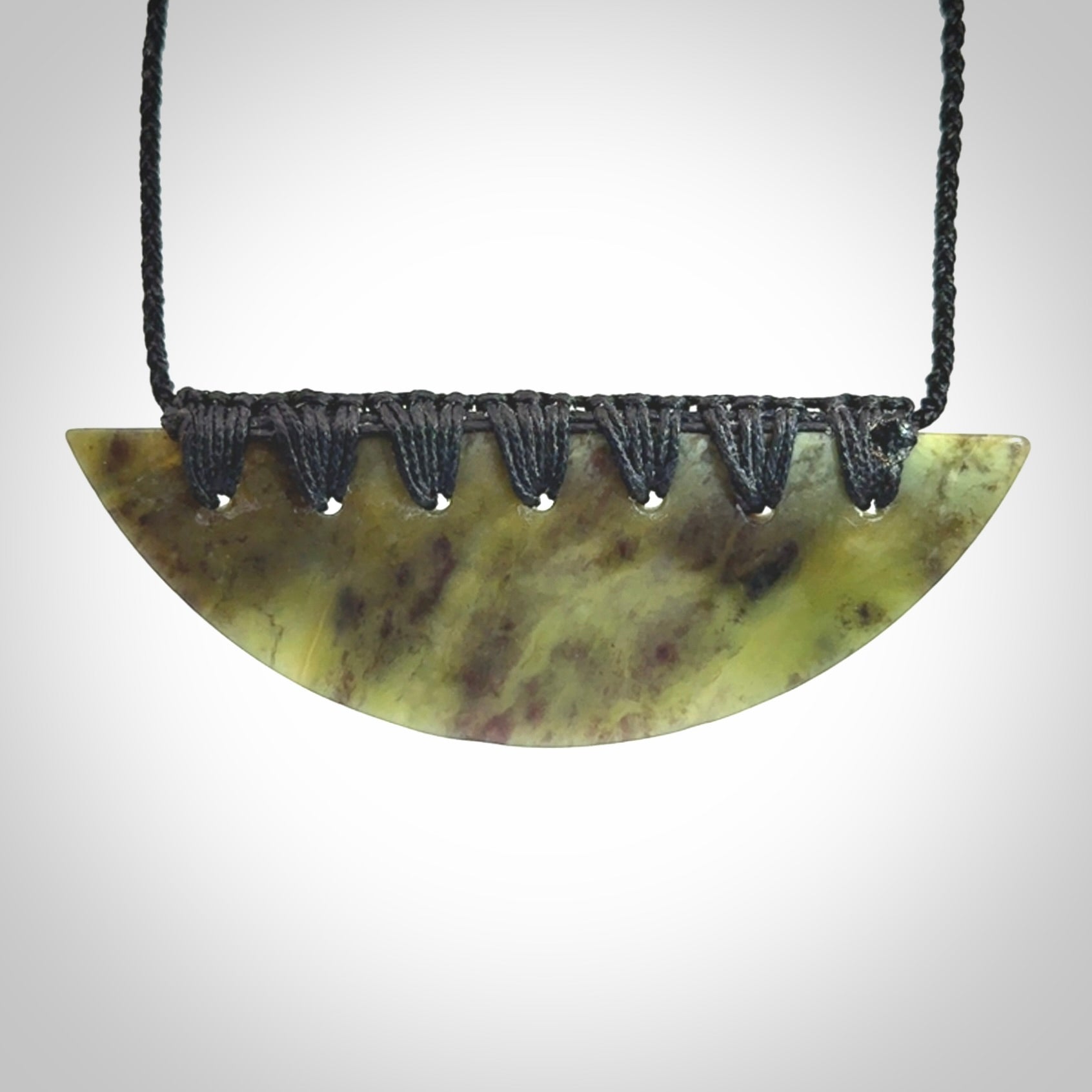 This picture shows a hand carved jade contemporary half-shield pendant. It is a semi-transluscent green colour. The cord is hand plaited and adjustable so that you can position the pendant where it suits you best.