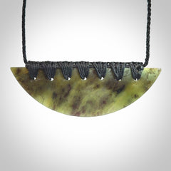 This picture shows a hand carved jade contemporary half-shield pendant. It is a semi-transluscent green colour. The cord is hand plaited and adjustable so that you can position the pendant where it suits you best.