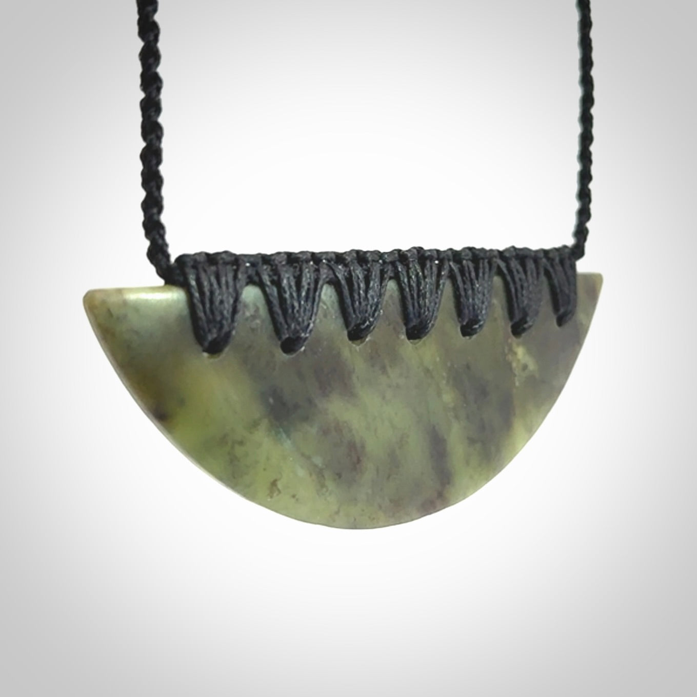 This picture shows a hand carved jade contemporary half-shield pendant. It is a semi-transluscent green colour. The cord is hand plaited and adjustable so that you can position the pendant where it suits you best.