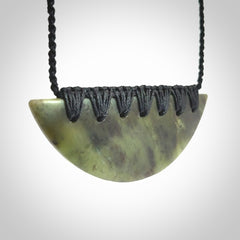 This picture shows a hand carved jade contemporary half-shield pendant. It is a semi-transluscent green colour. The cord is hand plaited and adjustable so that you can position the pendant where it suits you best.