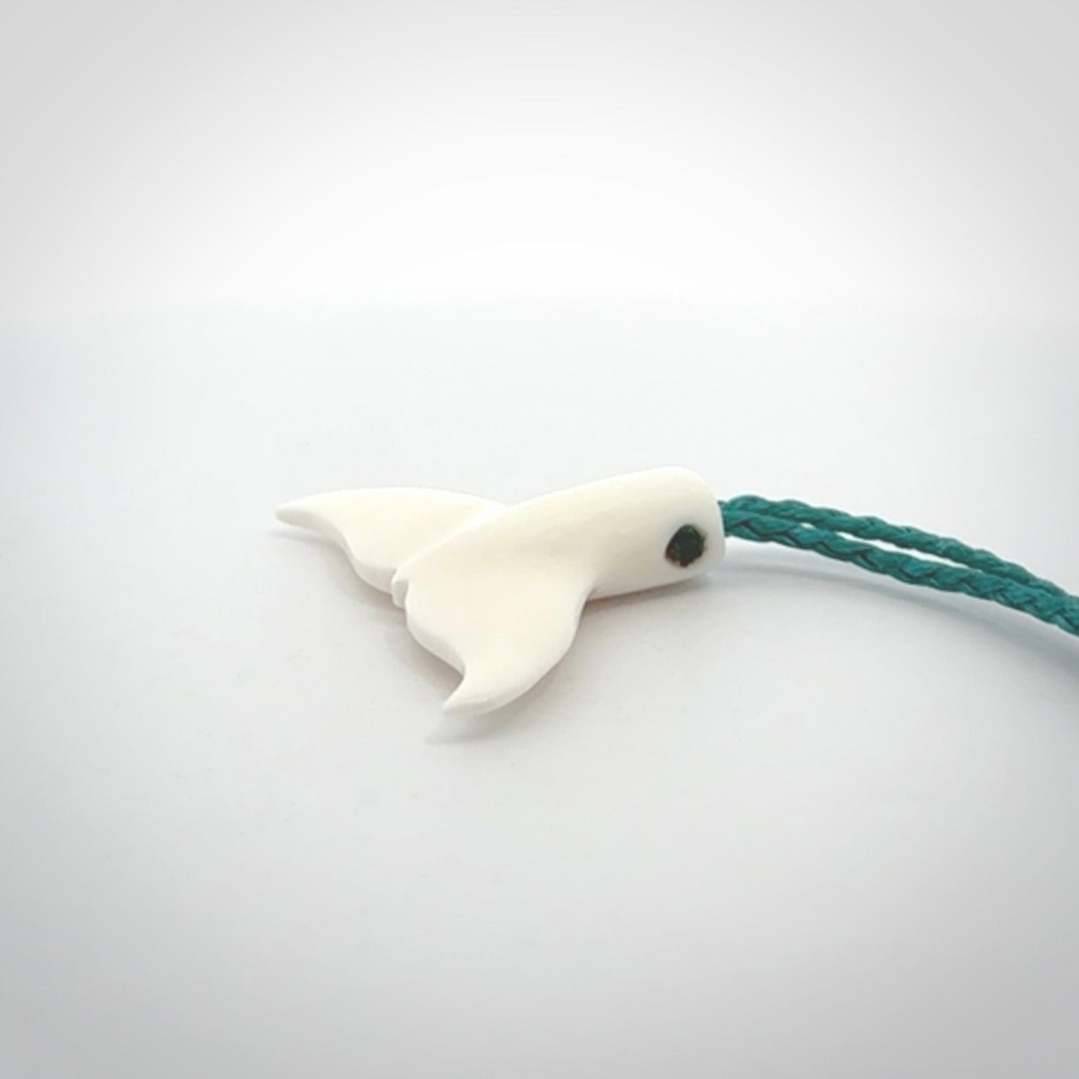 This is a lovely little Dolphin tail pendant. We have hand carved this in a bright, white bone and we make the necklace from a hand-plaited waxed cord. These are original NZ Pacific pendants, handmade from natural materials.