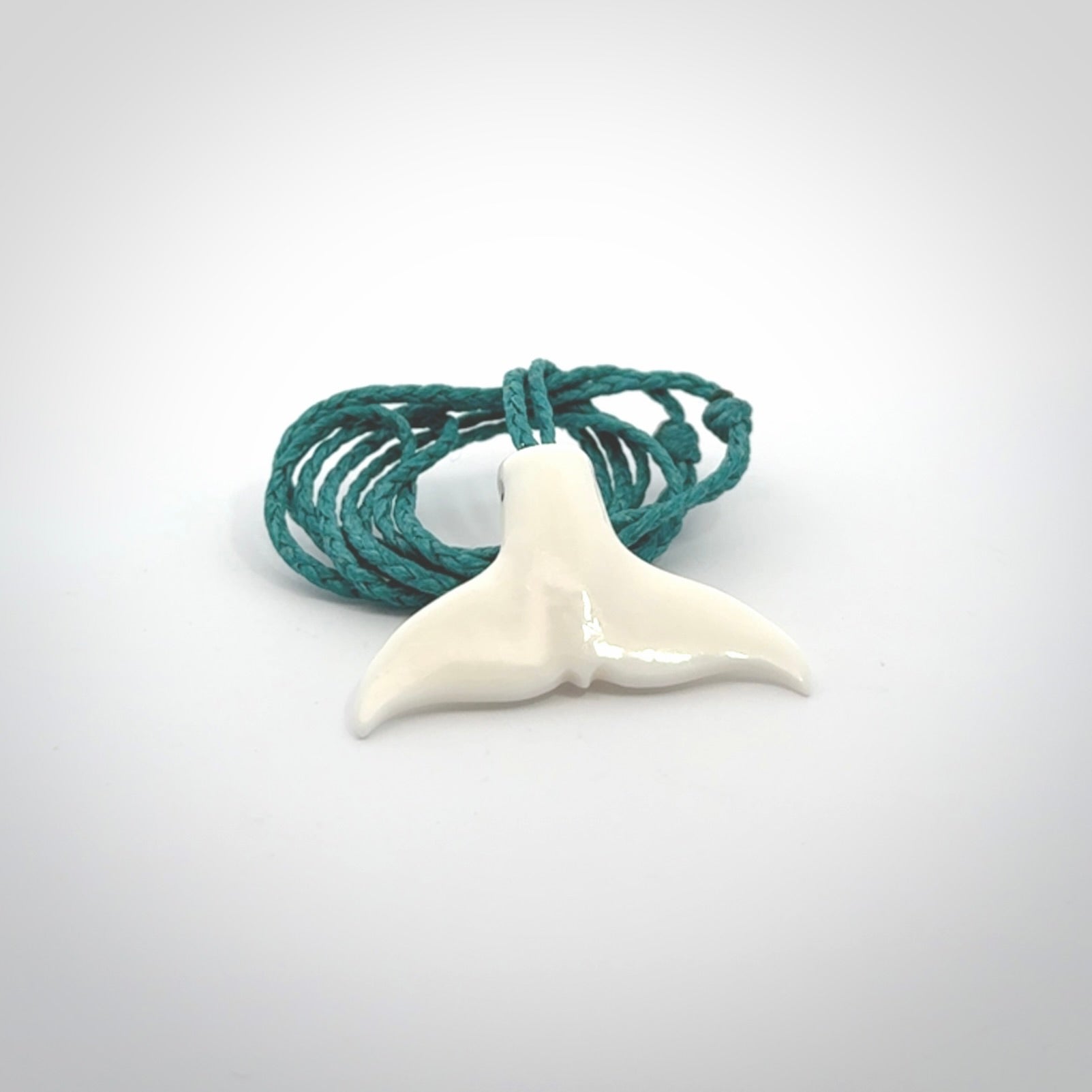 This is a lovely little Dolphin tail pendant. We have hand carved this in a bright, white bone and we make the necklace from a hand-plaited waxed cord. These are original NZ Pacific pendants, handmade from natural materials.