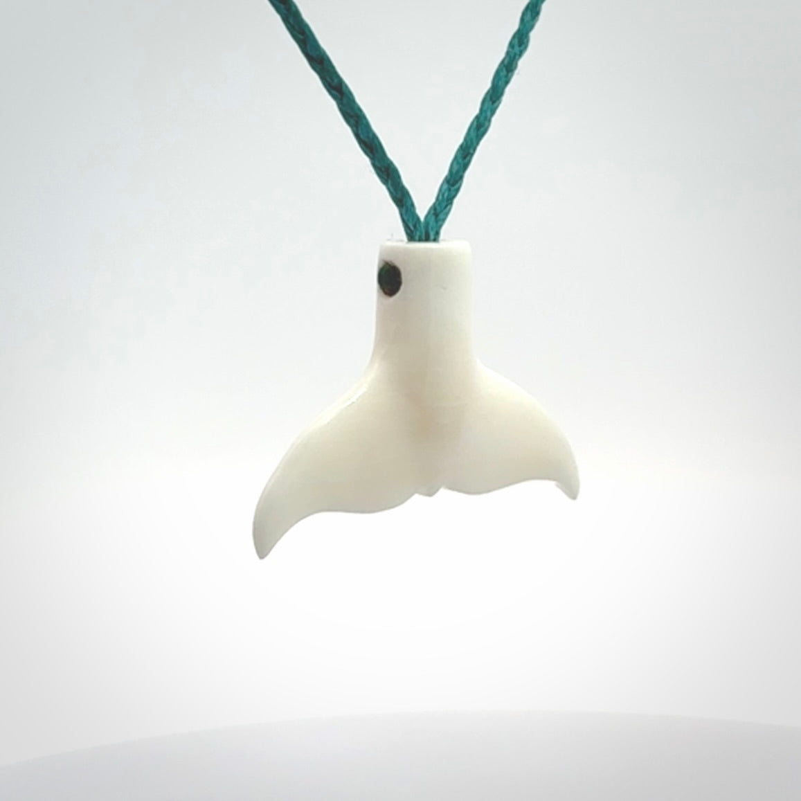 This is a lovely little Dolphin tail pendant. We have hand carved this in a bright, white bone and we make the necklace from a hand-plaited waxed cord. These are original NZ Pacific pendants, handmade from natural materials.