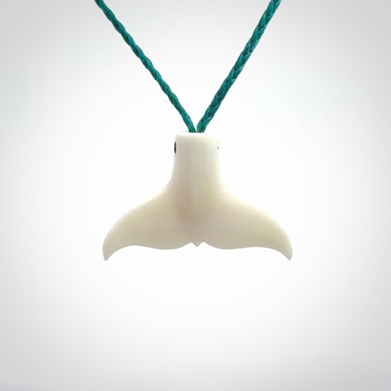 This is a lovely little Dolphin tail pendant. We have hand carved this in a bright, white bone and we make the necklace from a hand-plaited waxed cord. These are original NZ Pacific pendants, handmade from natural materials.