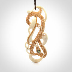 This picture shows a carved double manaia in bone. The artist has carved traditional decorative Koru designs into the face of the body and these run up the sides of the manaia head. These have specific meanings. It is provided with a hand-plaited brown cord that is length adjustable.