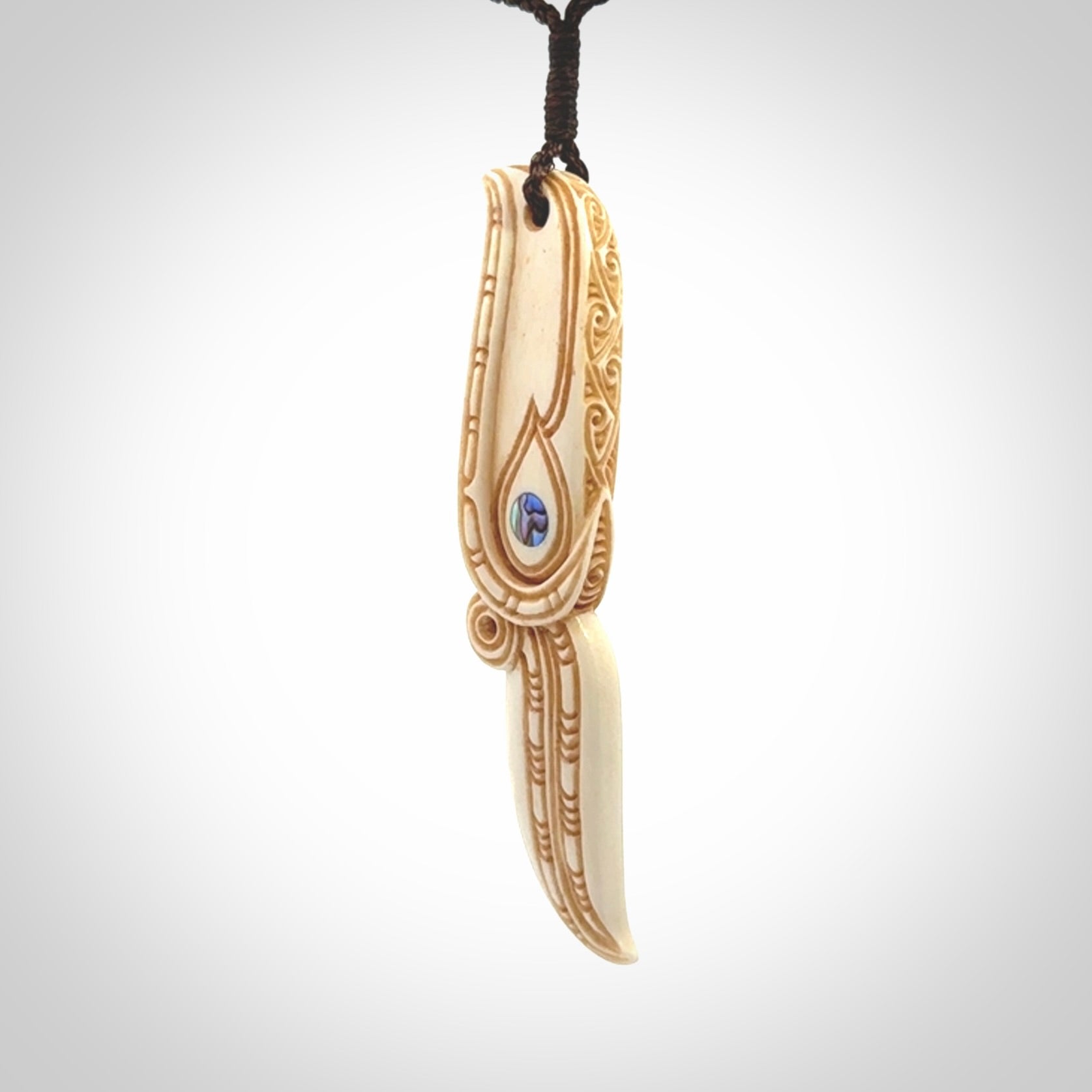 This picture shows a carved hawk in bone. It is a drop shaped pendant. The artist has carved traditional decorative kowhaiwhai designs into the body and these run up the sides of the hawk. These have specific meanings. It is provided with a hand-plaited brown cord that is length adjustable. Shipping is included and we ship worldwide.
