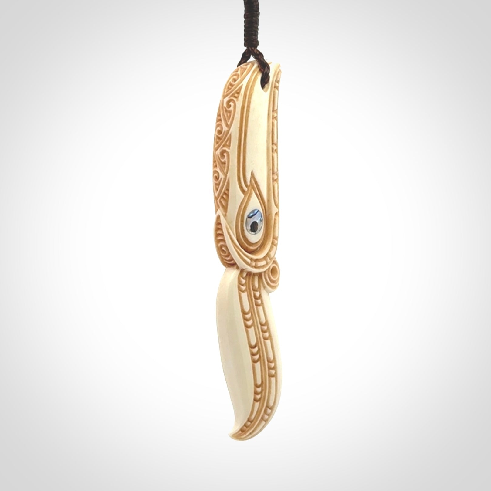 This picture shows a carved hawk in bone. It is a drop shaped pendant. The artist has carved traditional decorative kowhaiwhai designs into the body and these run up the sides of the hawk. These have specific meanings. It is provided with a hand-plaited brown cord that is length adjustable. Shipping is included and we ship worldwide.