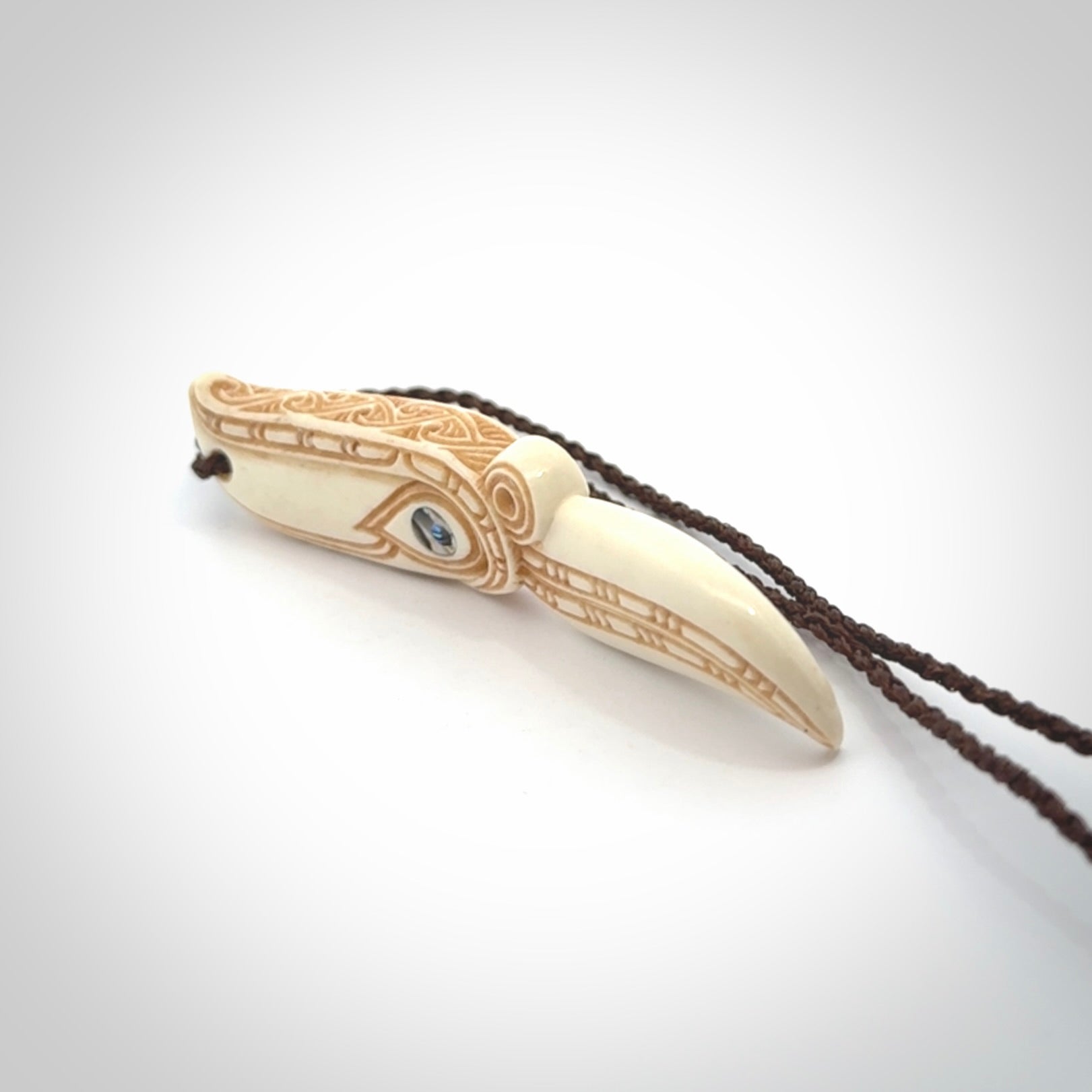 This picture shows a carved hawk in bone. It is a drop shaped pendant. The artist has carved traditional decorative kowhaiwhai designs into the body and these run up the sides of the hawk. These have specific meanings. It is provided with a hand-plaited brown cord that is length adjustable. Shipping is included and we ship worldwide.