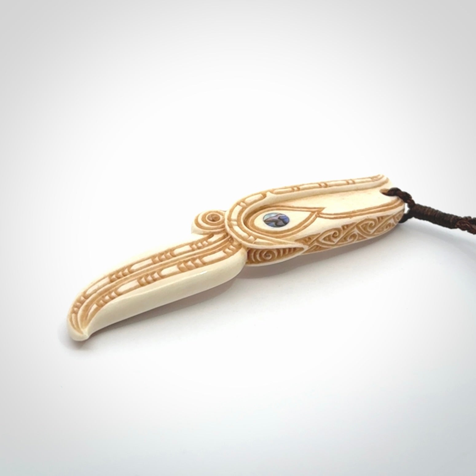 This picture shows a carved hawk in bone. It is a drop shaped pendant. The artist has carved traditional decorative kowhaiwhai designs into the body and these run up the sides of the hawk. These have specific meanings. It is provided with a hand-plaited brown cord that is length adjustable. Shipping is included and we ship worldwide.