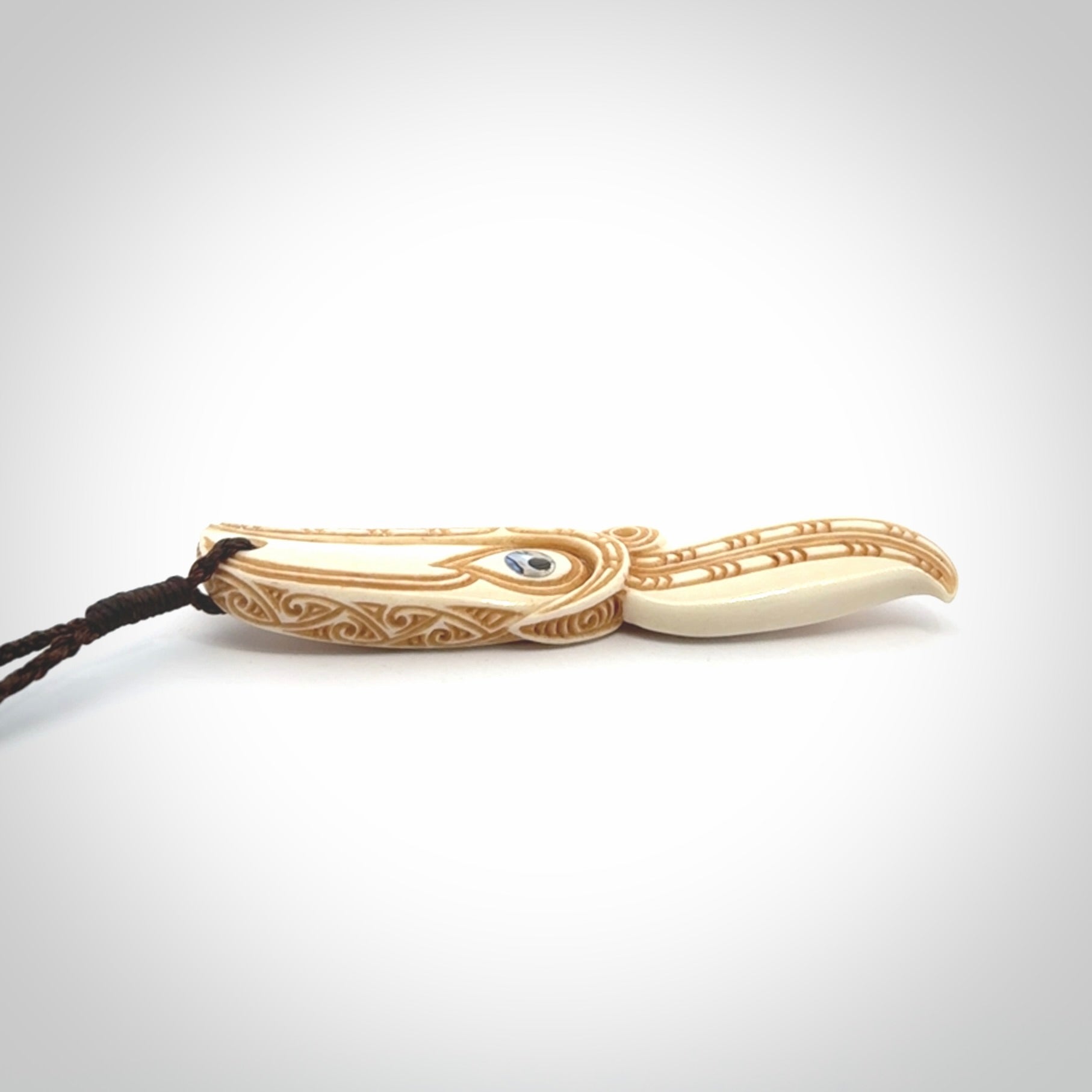 This picture shows a carved hawk in bone. It is a drop shaped pendant. The artist has carved traditional decorative kowhaiwhai designs into the body and these run up the sides of the hawk. These have specific meanings. It is provided with a hand-plaited brown cord that is length adjustable. Shipping is included and we ship worldwide.