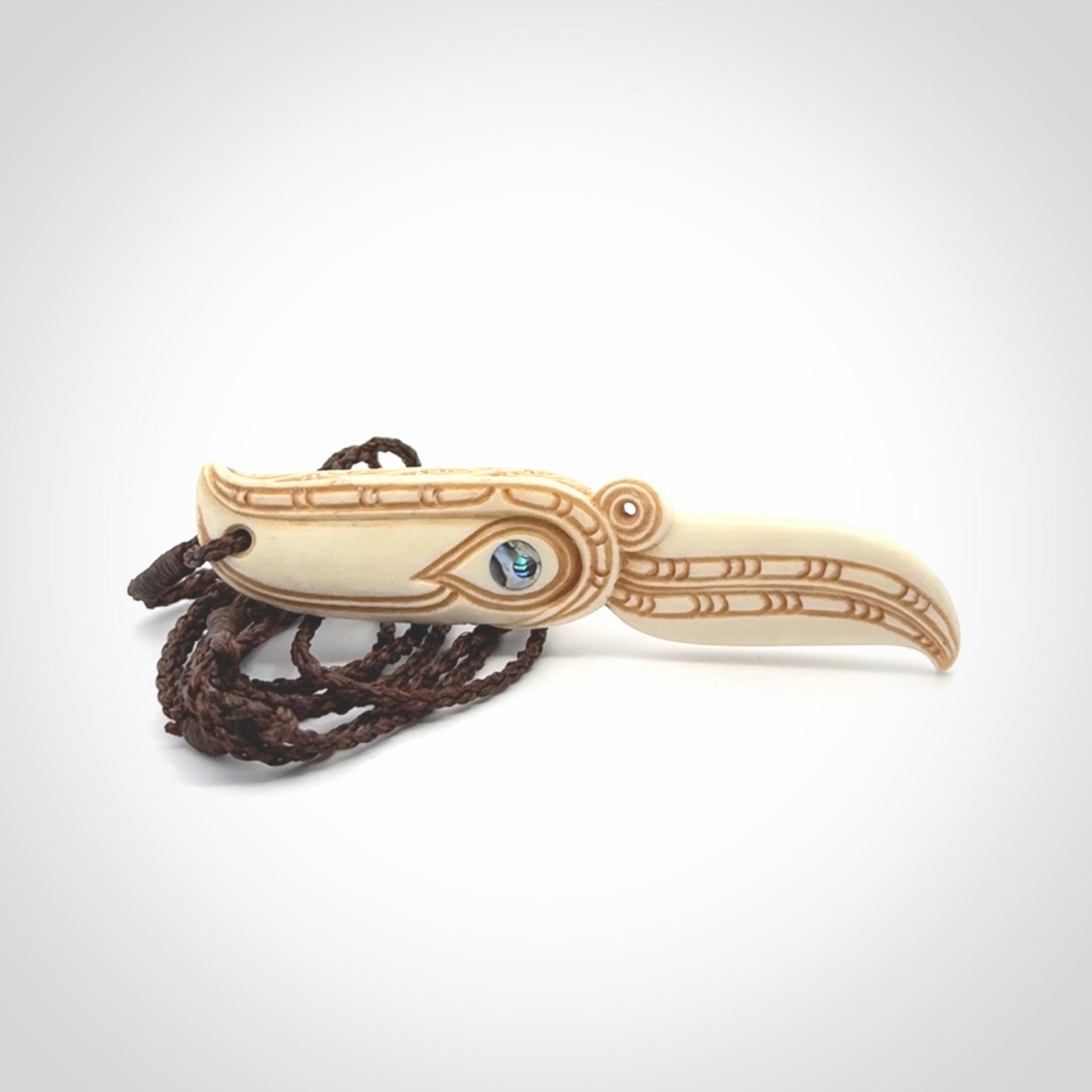 This picture shows a carved hawk in bone. It is a drop shaped pendant. The artist has carved traditional decorative kowhaiwhai designs into the body and these run up the sides of the hawk. These have specific meanings. It is provided with a hand-plaited brown cord that is length adjustable. Shipping is included and we ship worldwide.