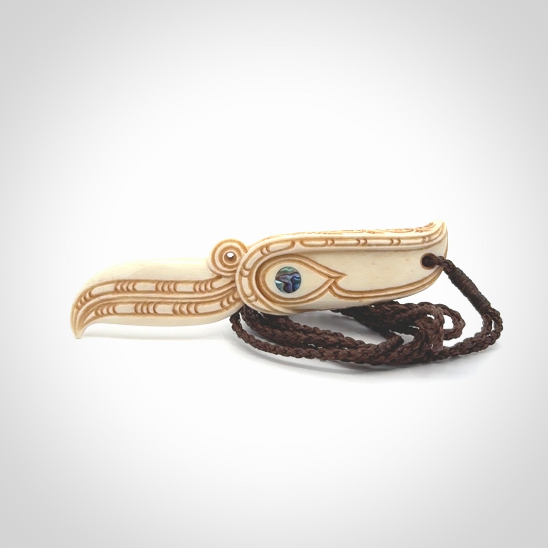 This picture shows a carved hawk in bone. It is a drop shaped pendant. The artist has carved traditional decorative kowhaiwhai designs into the body and these run up the sides of the hawk. These have specific meanings. It is provided with a hand-plaited brown cord that is length adjustable. Shipping is included and we ship worldwide.